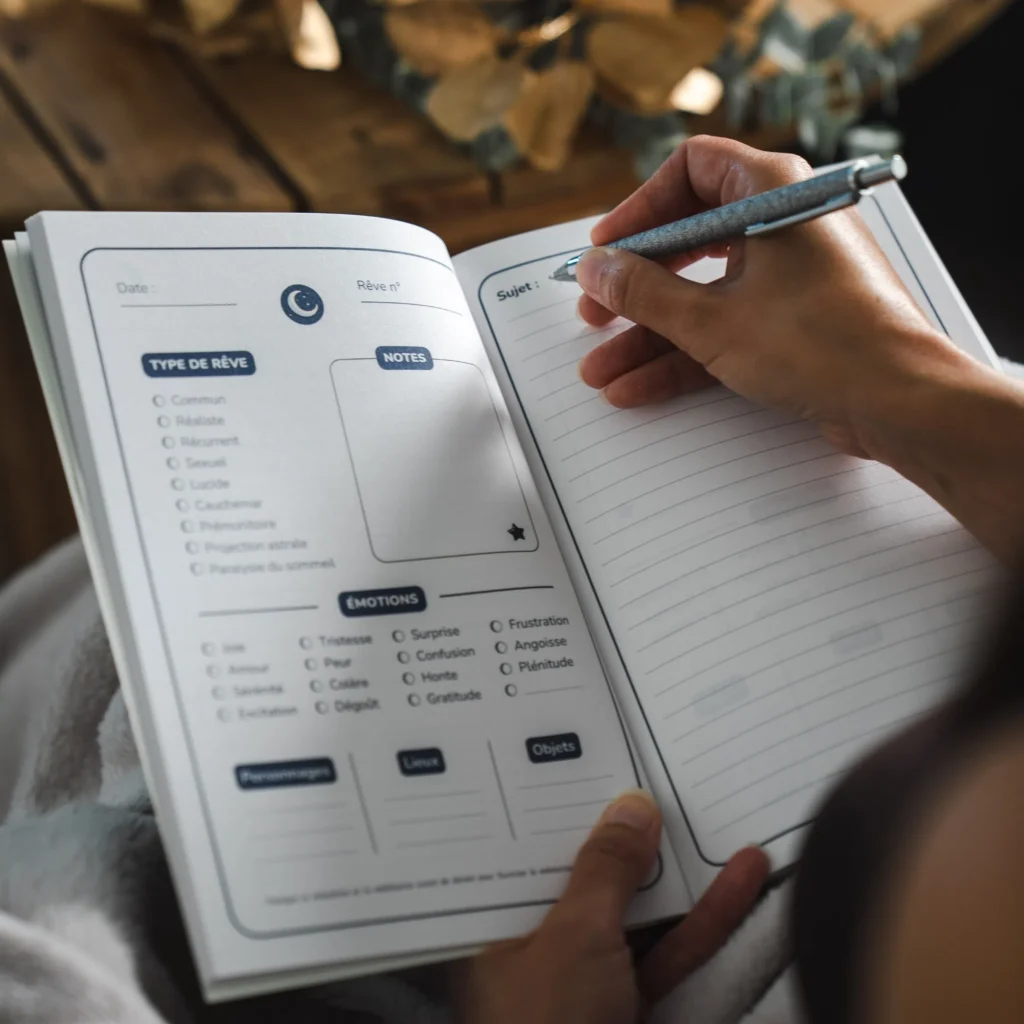 Main écrivant dans le Journal de Rêves avec stylo, montrant l'utilisation pratique des pages structurées pour noter ses rêves au réveil